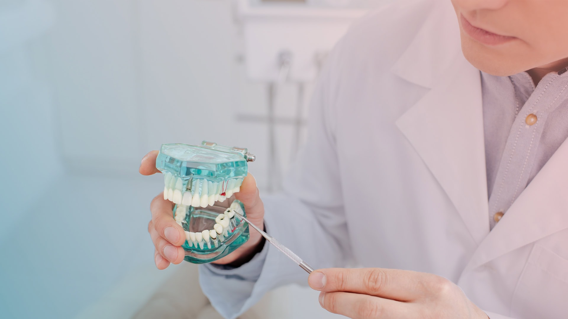 Beyaz önlüklü diş hekiminin şeffaf implantlı çene modeli tutup sondla işaret etmesi
