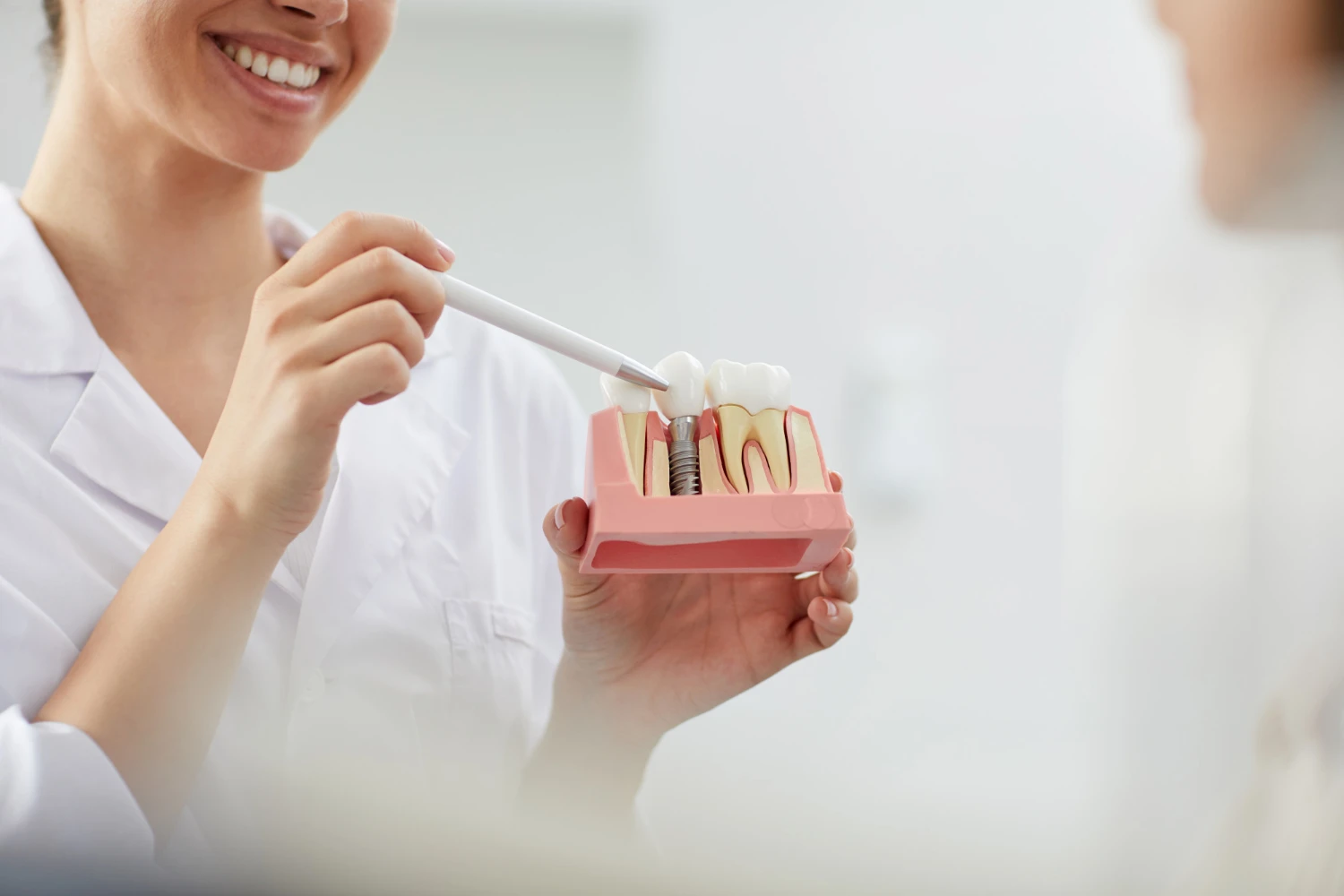 Bir elinde implant eğitim modeli tutarken modele işaret eden diş hekimi