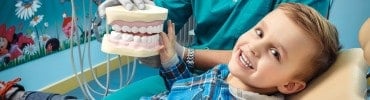 Hekim elindeki büyük diş modelini çocuğa gösteriyor, bulanık yakın çekim