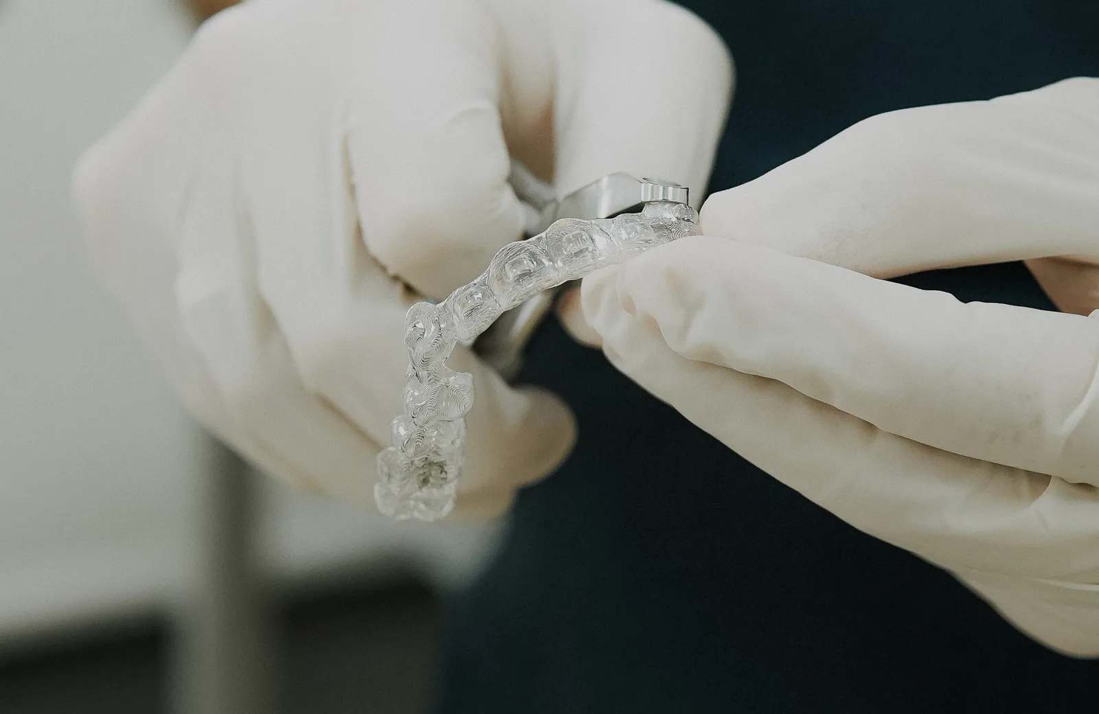 Beyaz eldivenli iki el şeffaf bir plağı tutuyor, bir elde plağın kenarına değen metal bir pens var