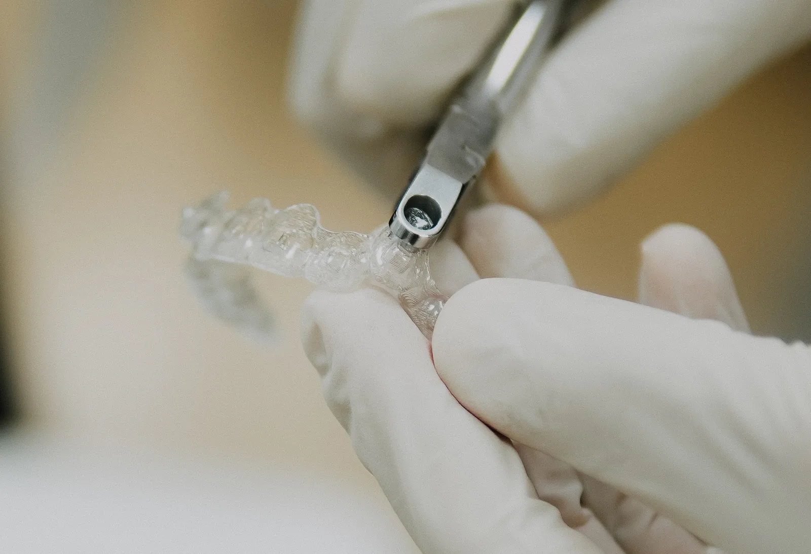 Gloved hands trimming the edge of a clear aligner with a metal instrument